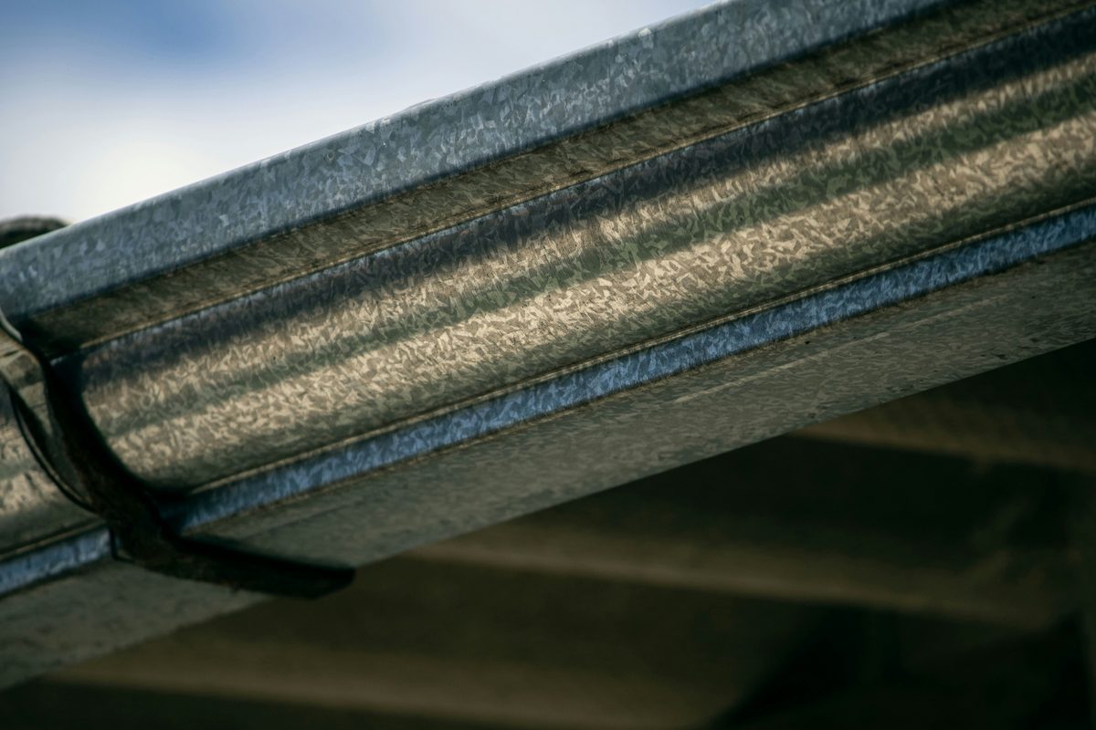 Close view of a gutter and the metal hanger strap holding it to the roof edge